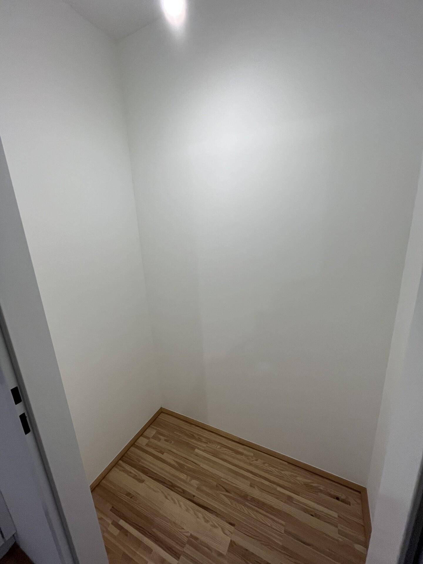 Leerer Abstellraum mit hellen Wänden und Holzfußboden, ideal für zusätzlichen Stauraum.