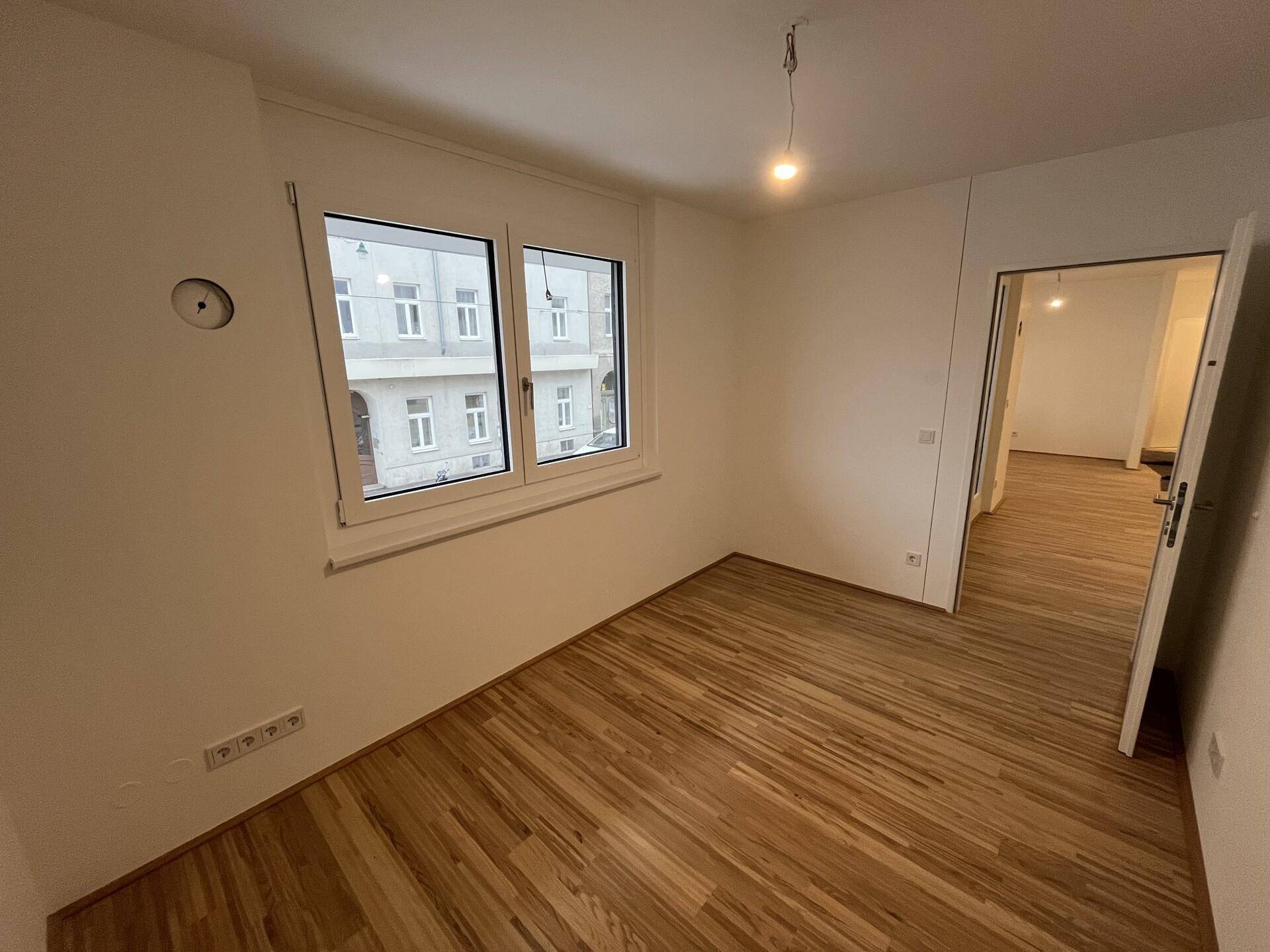 Helles Zimmer mit Holzfußboden und Blick auf die gegenüberliegenden Gebäude der Stadt.