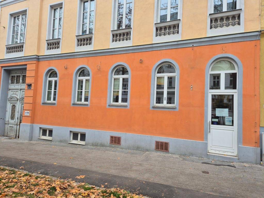 Fassade eines Gebäudes mit orangefarbenem Erdgeschoss, Rundbogenfenstern und gelben Obergeschossen mit Balkonen.