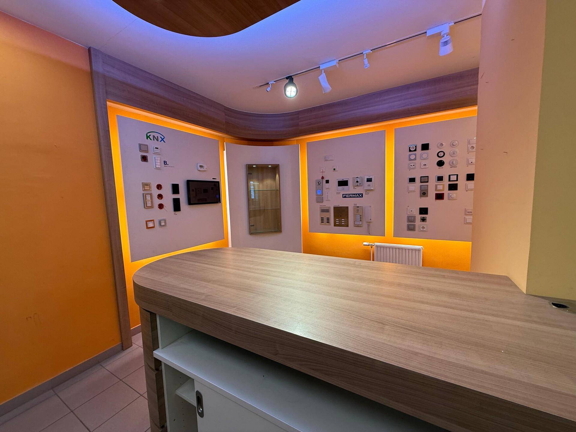 Moderner Ausstellungsraum mit Holztresen und beleuchteten Wandpaneelen, die verschiedene Schalter und Bedienelemente präsentieren.