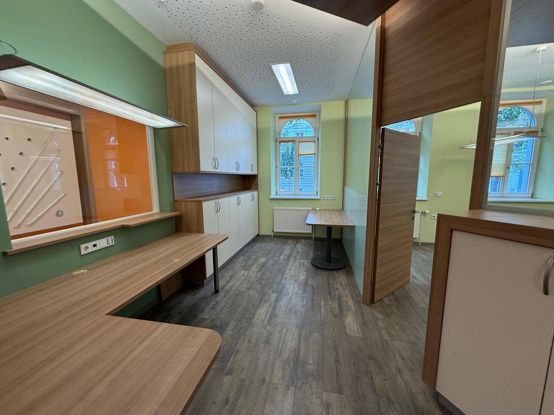 Helles Büro mit integrierten Schränken, Arbeitsplätzen und Holzoptik-Laminatboden, ideal für konzentriertes Arbeiten.