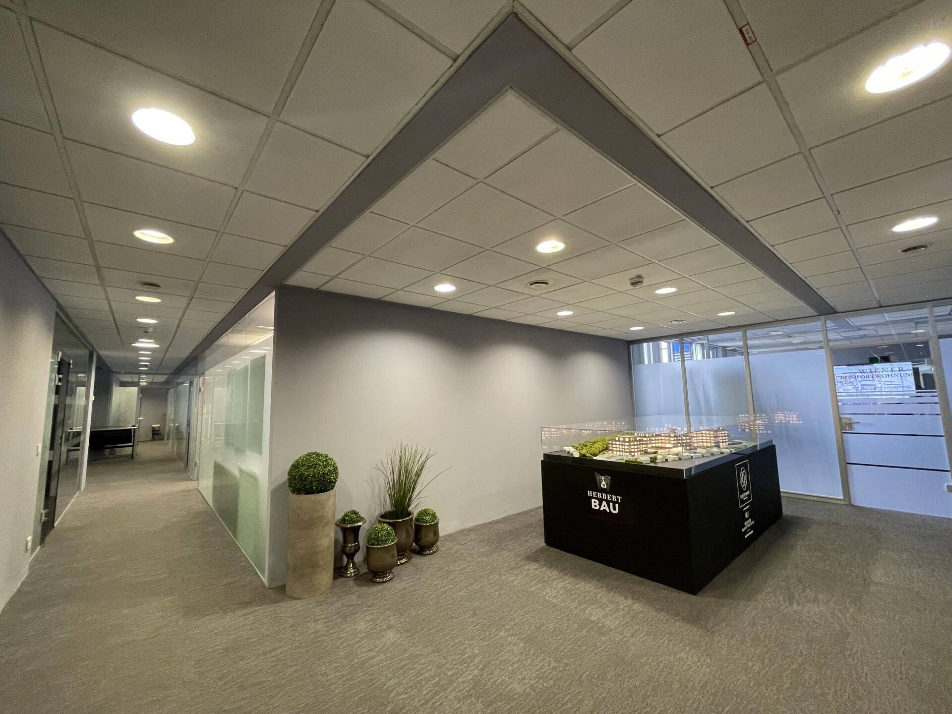 Heller Bürogang mit Teppichboden, Glaswänden und einem Modell einer Immobilienentwicklung.
