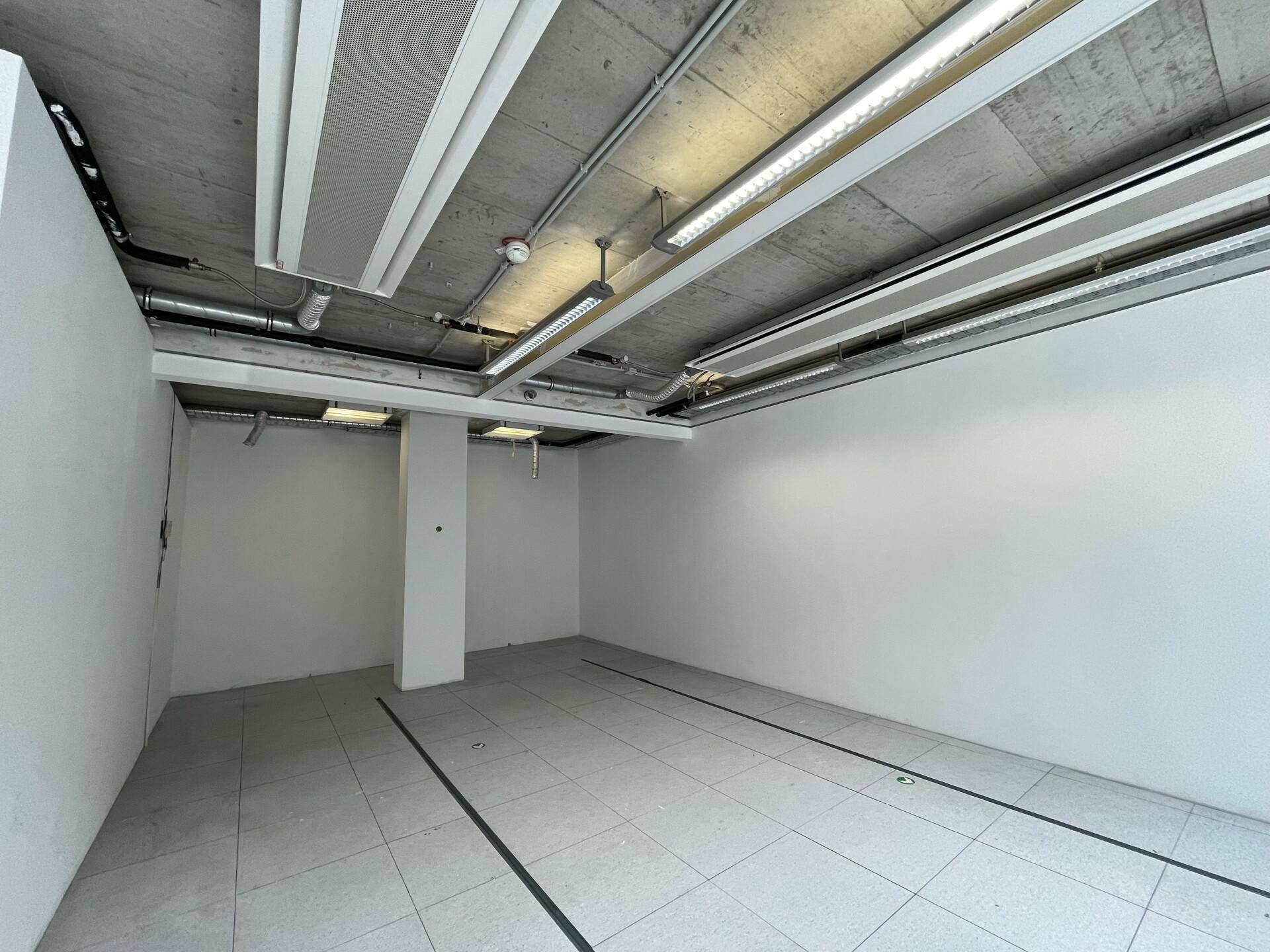 Leerer Büroraum mit Fliesenboden, weißen Wänden und sichtbaren Lüftungsrohren an der Decke.
