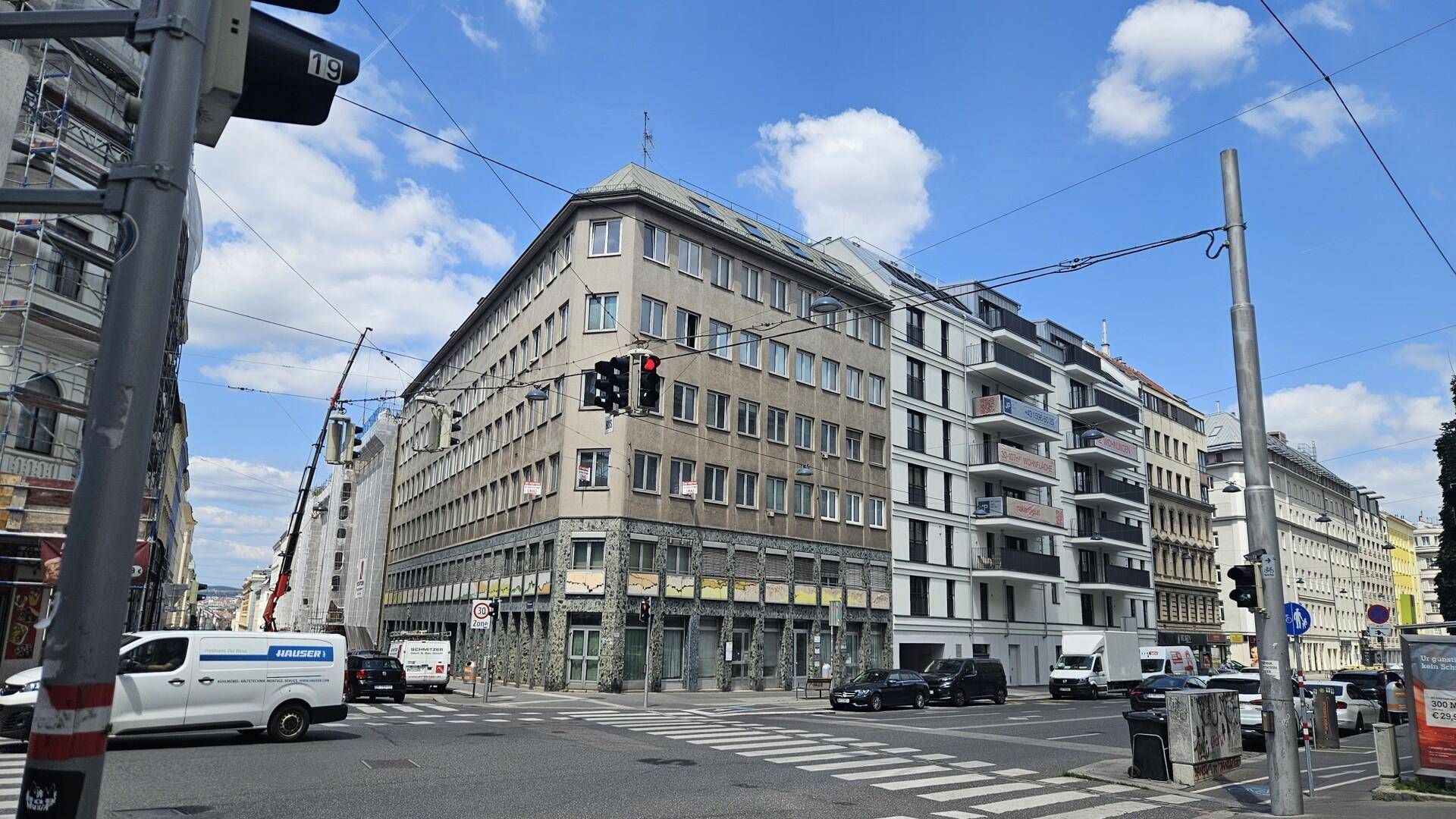 Gebäude an einer belebten Kreuzung mit verschiedenen Architekturstilen unter blauem Himmel.