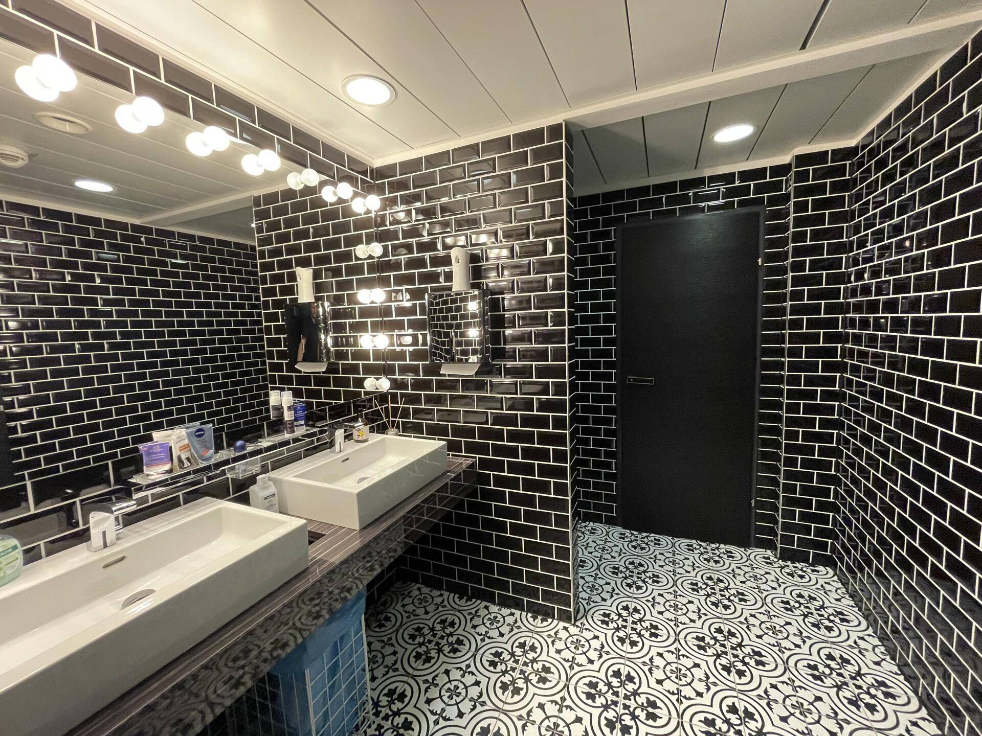 Modernes Badezimmer mit schwarzen U-Bahn-Fliesen, zwei Waschbecken und dekorativem Bodenmuster.