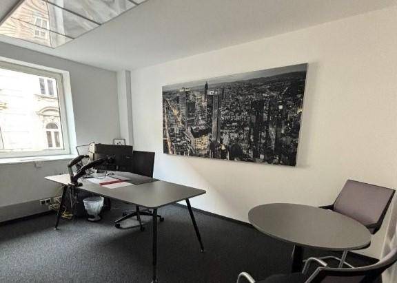 Einzelbüro mit Schreibtisch, Stühlen und einem großen Schwarz-Weiß-Bild der Stadt an der Wand.