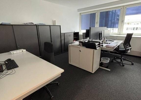 Modernes Büro mit mehreren Arbeitsplätzen, dunklen Schränken und großen Fenstern für viel Tageslicht.