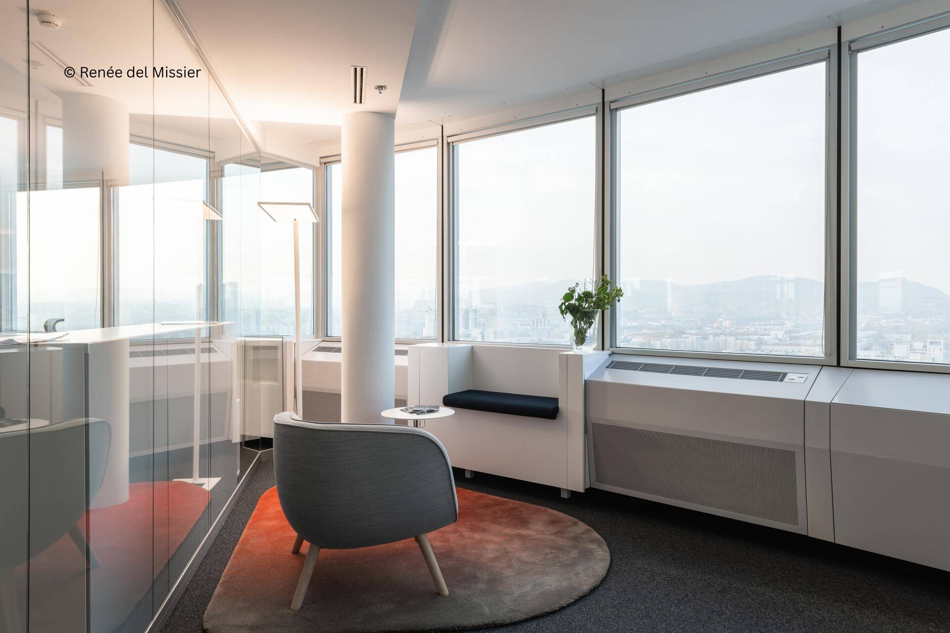Gemütliche Sitzecke im Büro mit großen Fenstern, die einen weiten Blick über die Stadt bieten.
