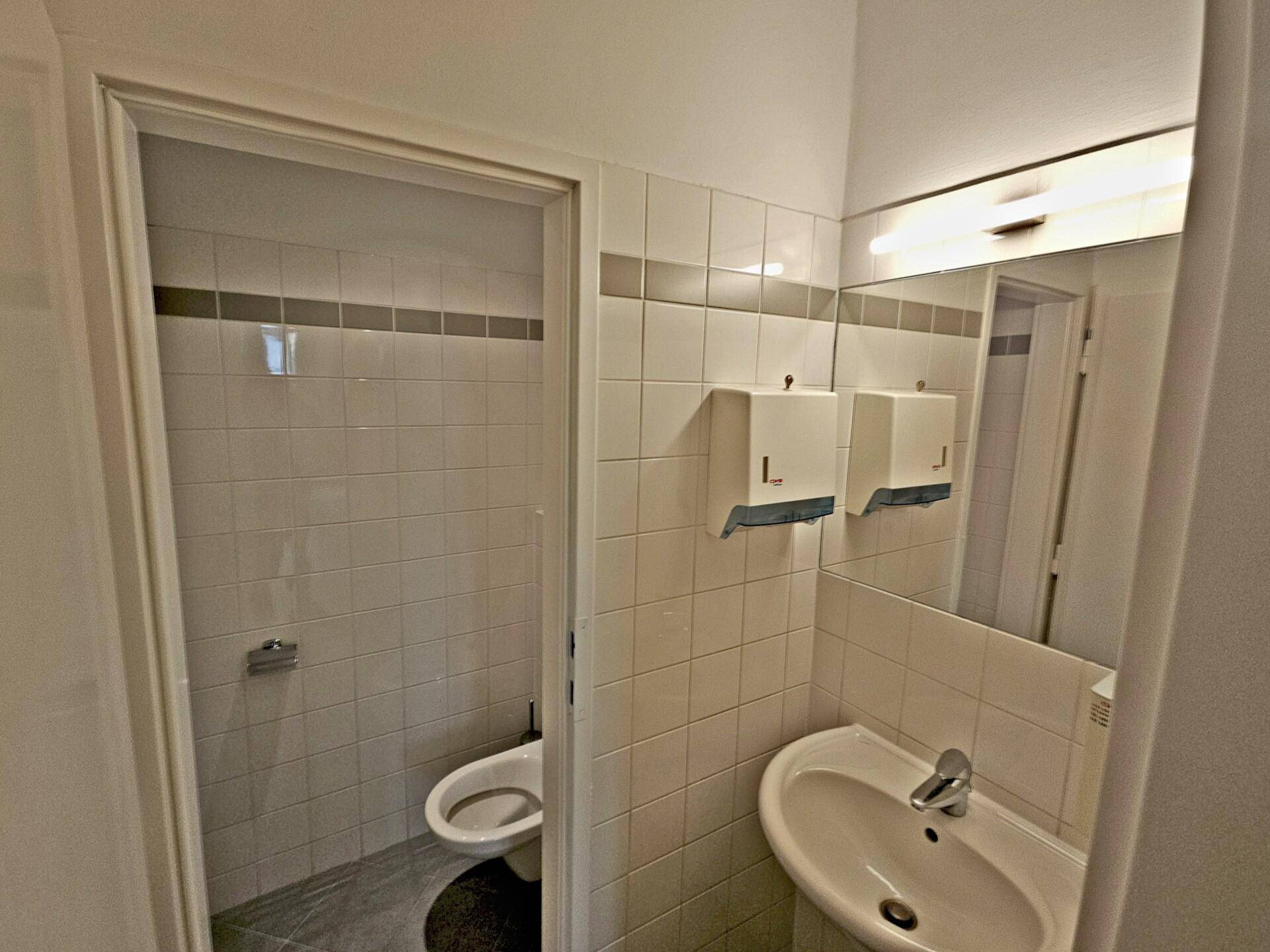 Einfache Toilette mit Waschbecken und Fliesen an den Wänden, funktional und sauber.