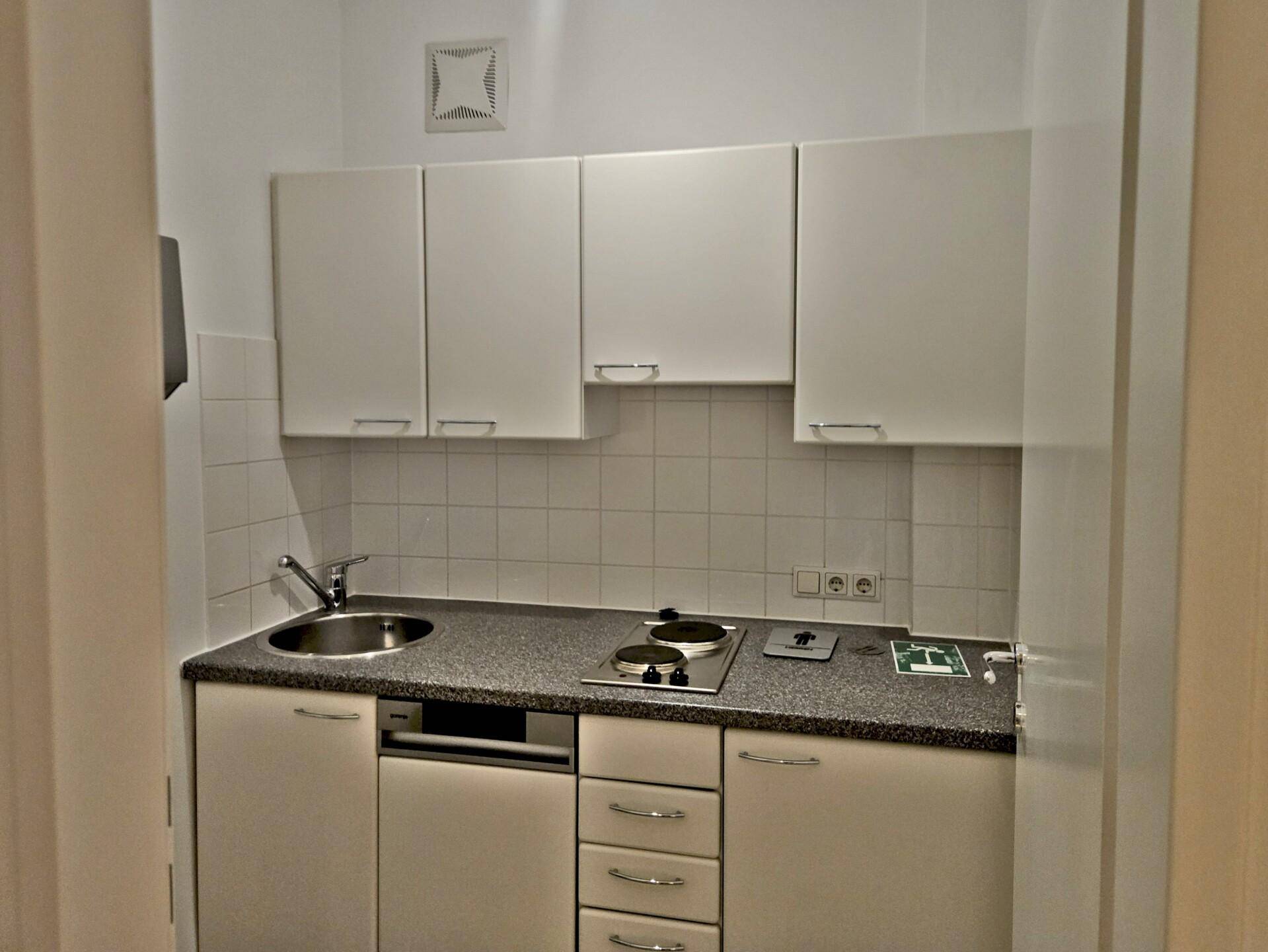 Kleine Einbauküche mit weißen Schränken, Spüle und zwei Kochplatten, ideal für eine Einzelperson.