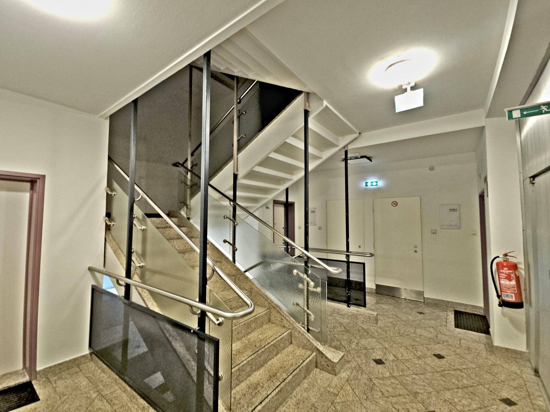 Modernes Treppenhaus mit Steinstufen, Glasgeländer und Edelstahlhandläufen in einem Mehrfamilienhaus.