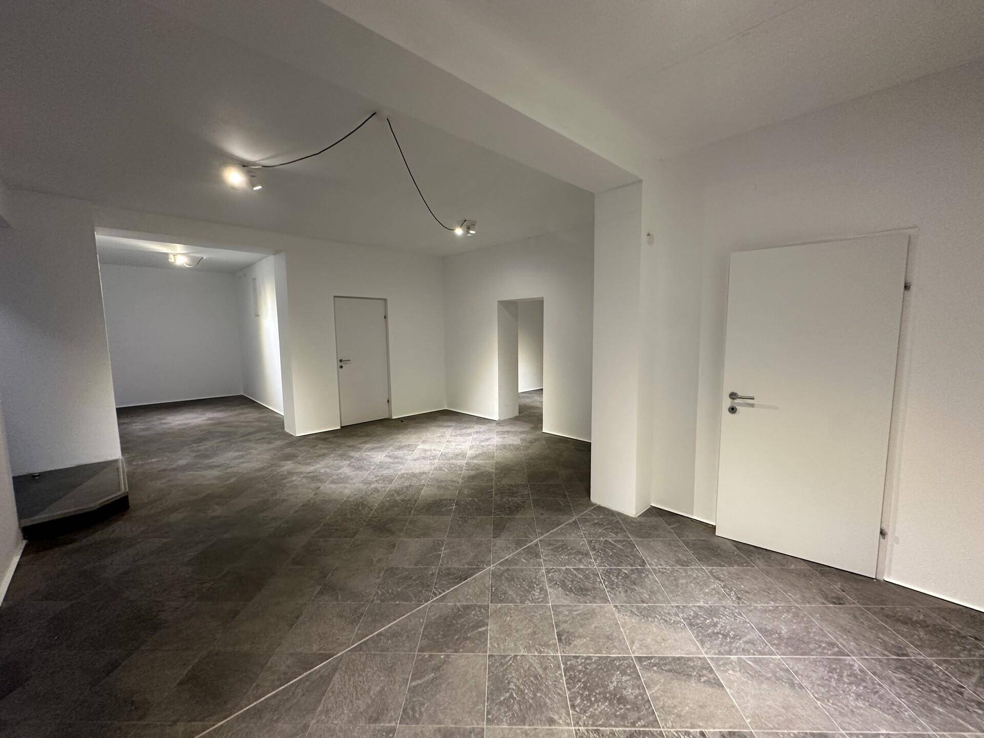 Weitläufiger Geschäftsraum mit dunklem Fliesenboden und mehreren Türen, die zu weiteren Bereichen innerhalb des Lokals führen.
