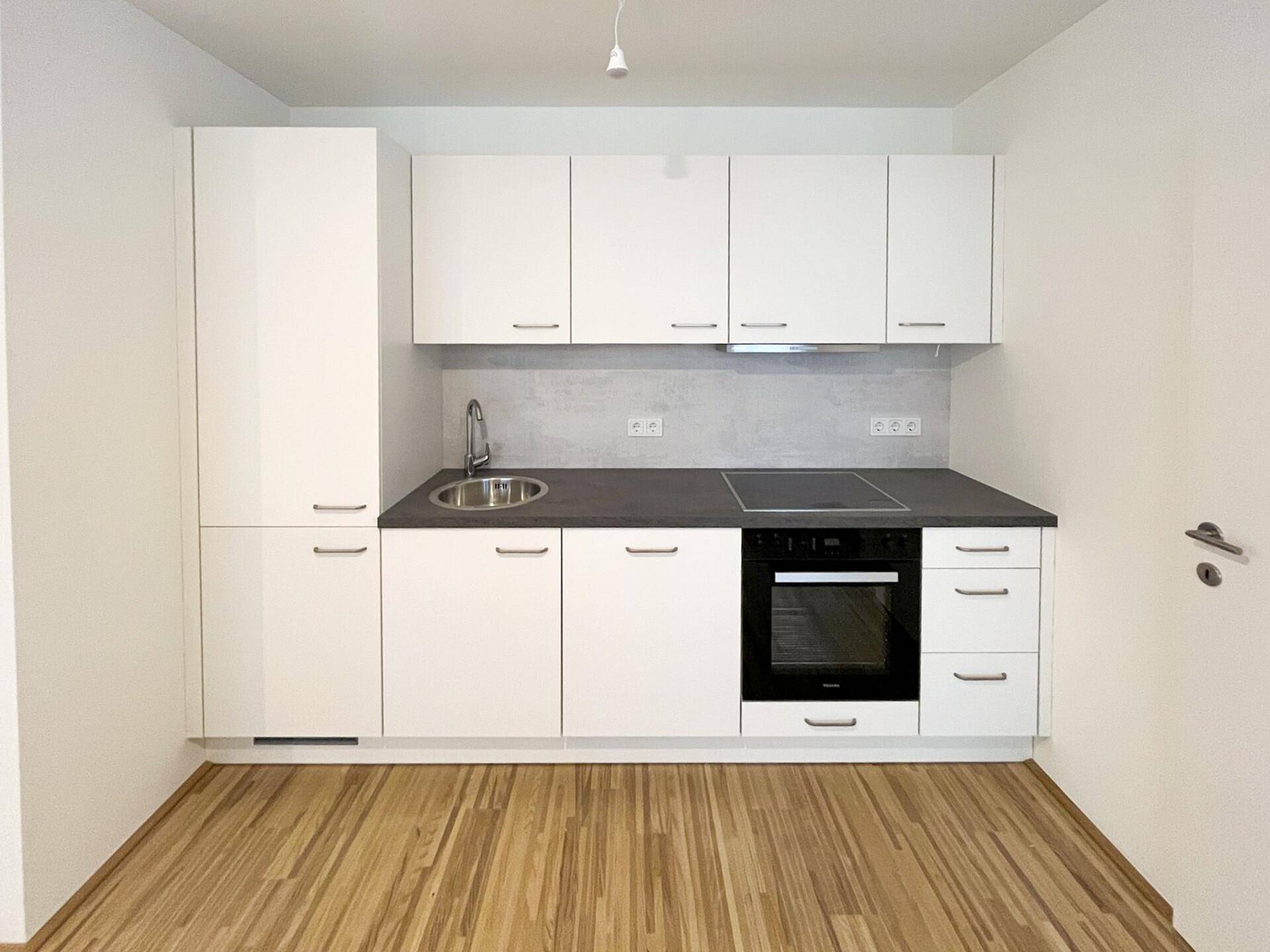 Moderne Einbauküche mit weißen Schränken, dunkler Arbeitsplatte und integrierten Geräten.