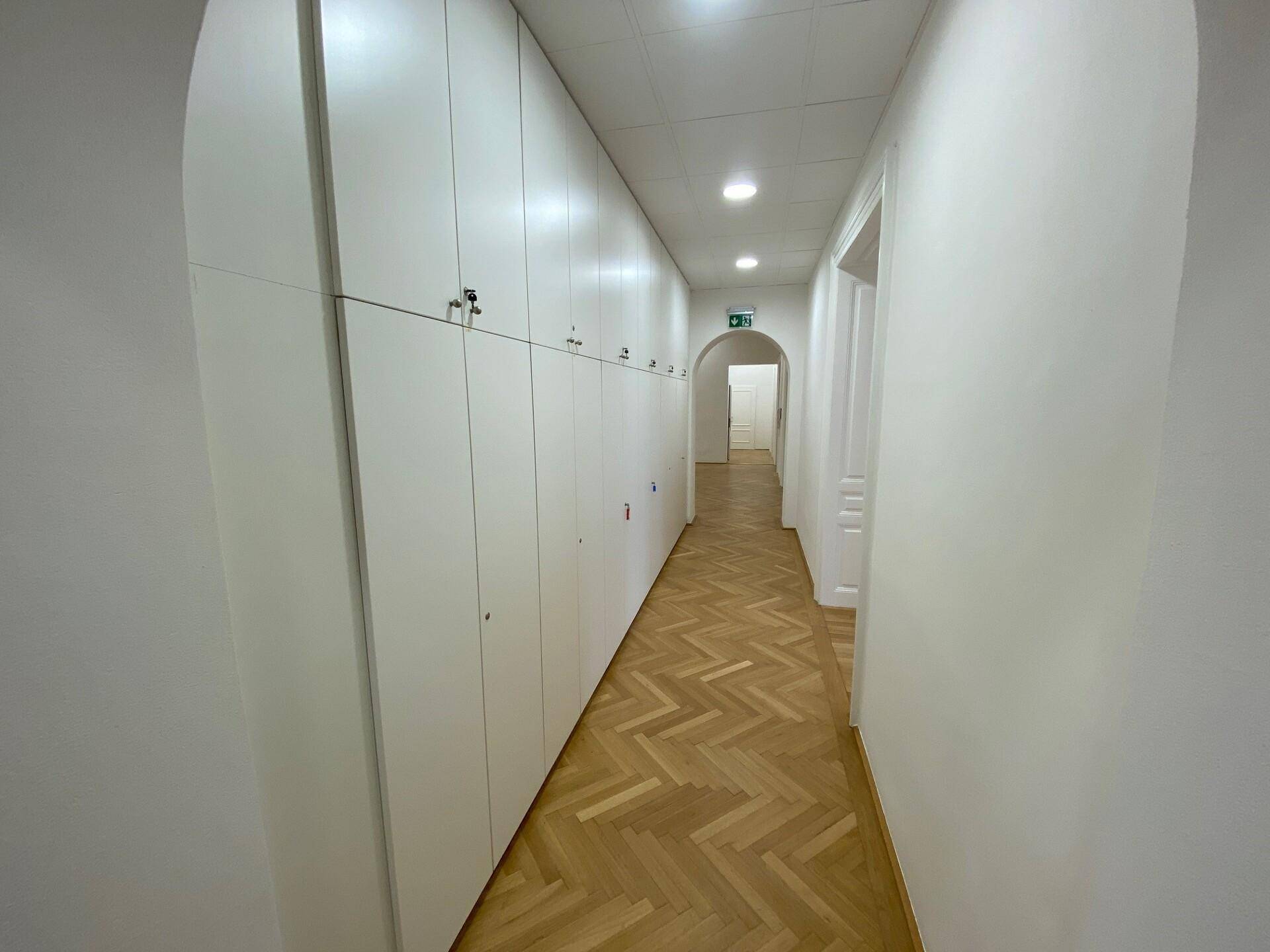 Langer Flur mit durchgehendem Fischgrätparkett und einer Wand voller weißer, hoher Einbauschränke.