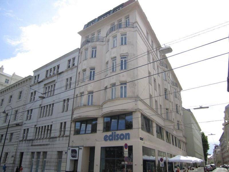Modernes Gebäude mit geschwungener Fassade, großen Fenstern und einem Geschäft im Erdgeschoss in urbaner Umgebung.