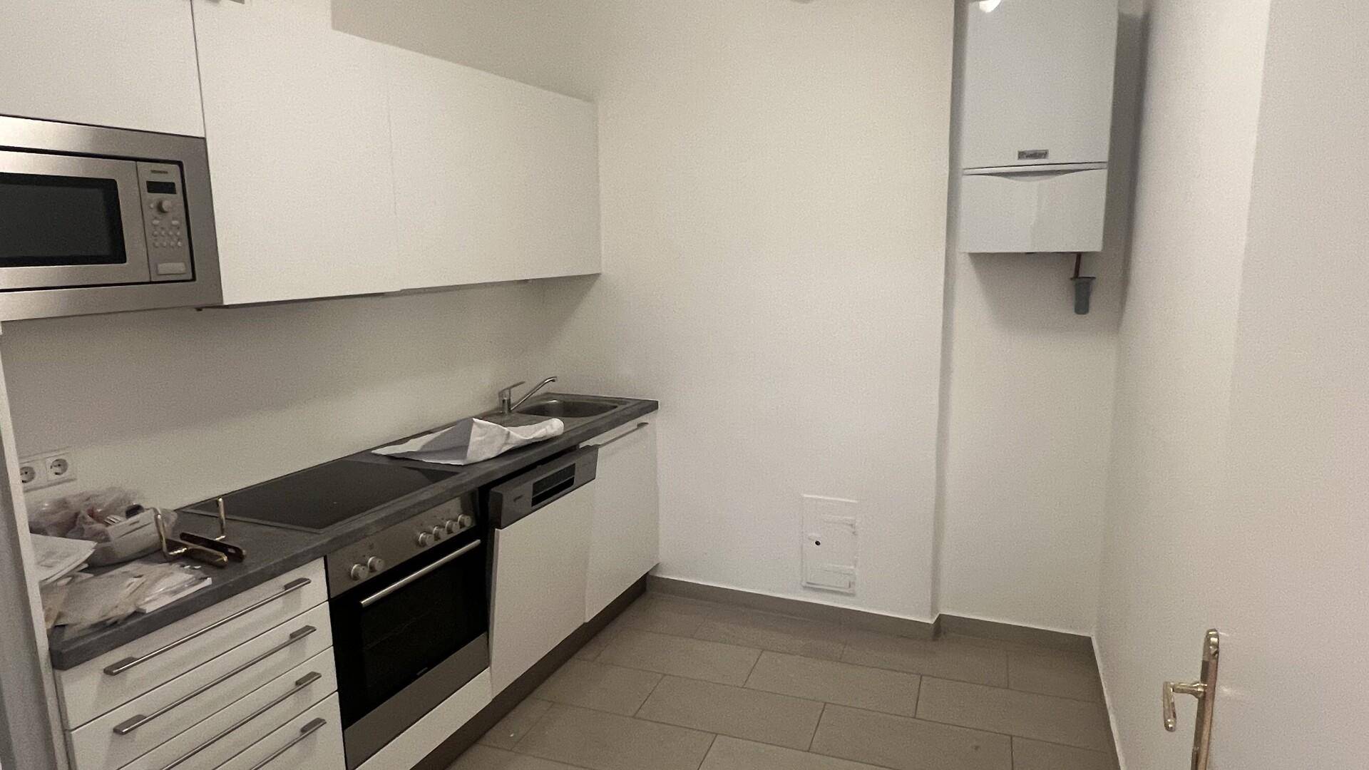 Kompakte, moderne Küche mit weißen Schränken, integrierten Geräten und Fliesenboden.