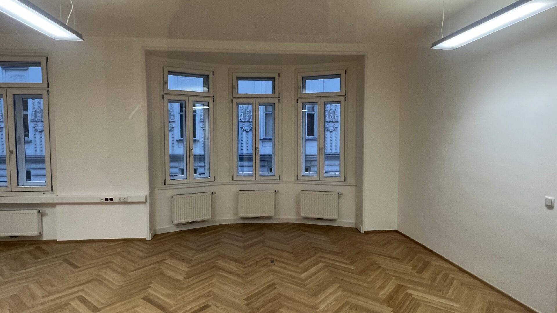 Heller Raum mit großen Bogenfenstern und klassischem Fischgrätparkett, der eine offene und einladende Atmosphäre bietet.