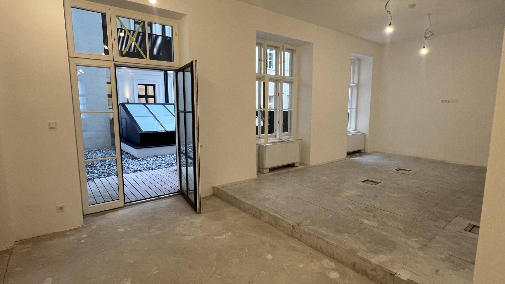Heller Raum mit Zugang zu einem Außenbereich und Blick auf ein modernes Glasdach.