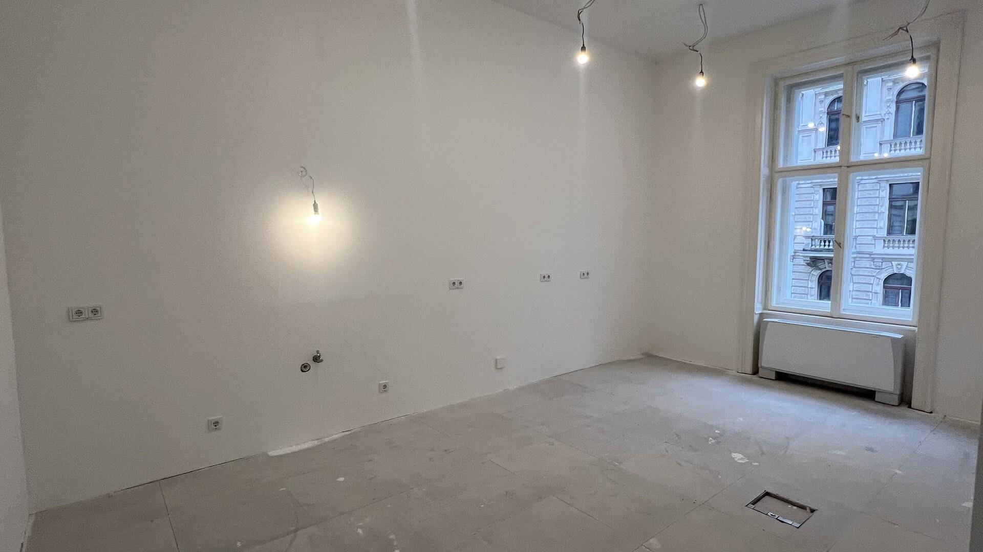 Heller Raum mit großen Fenstern, weißen Wänden und vorbereiteten Anschlüssen für die Elektroinstallation.