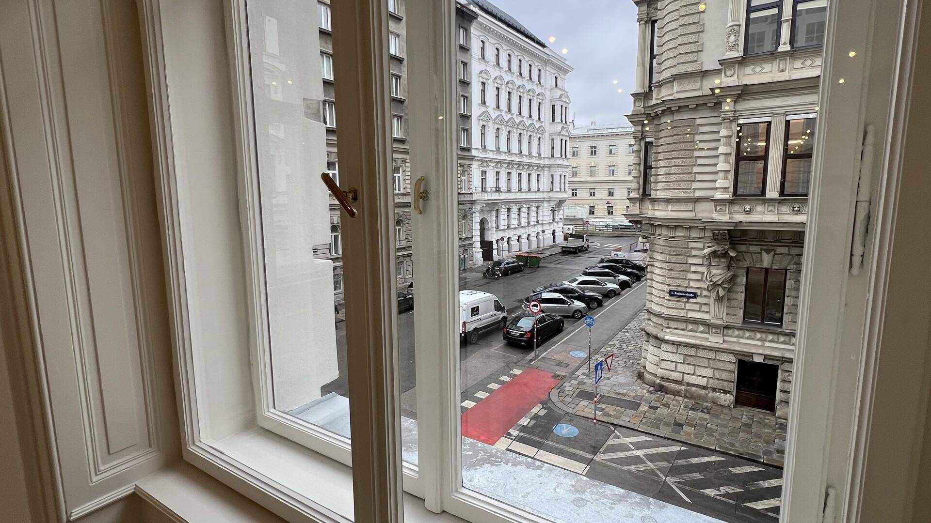 Blick aus dem Fenster auf eine belebte Stadtstraße mit parkenden Autos und historischen Gebäuden.