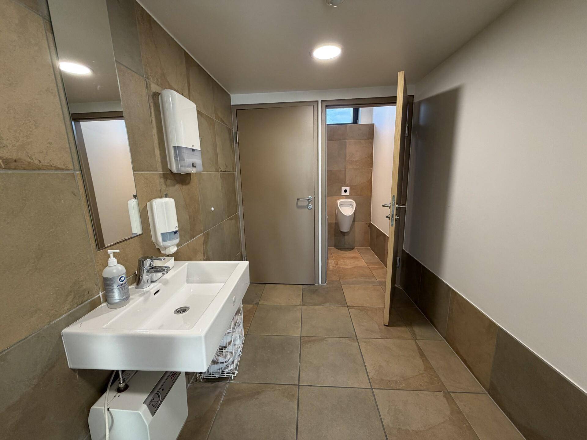 Modernes Badezimmer mit Urinal, Waschbecken und Fliesen in Erdtönen.