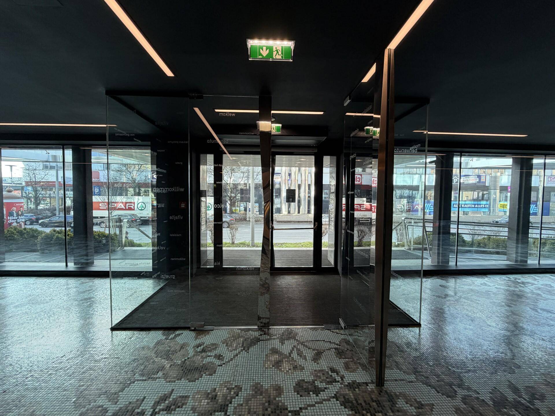 Moderner Eingangsbereich mit Glaswänden, Mosaikboden und Blick auf die Straße.