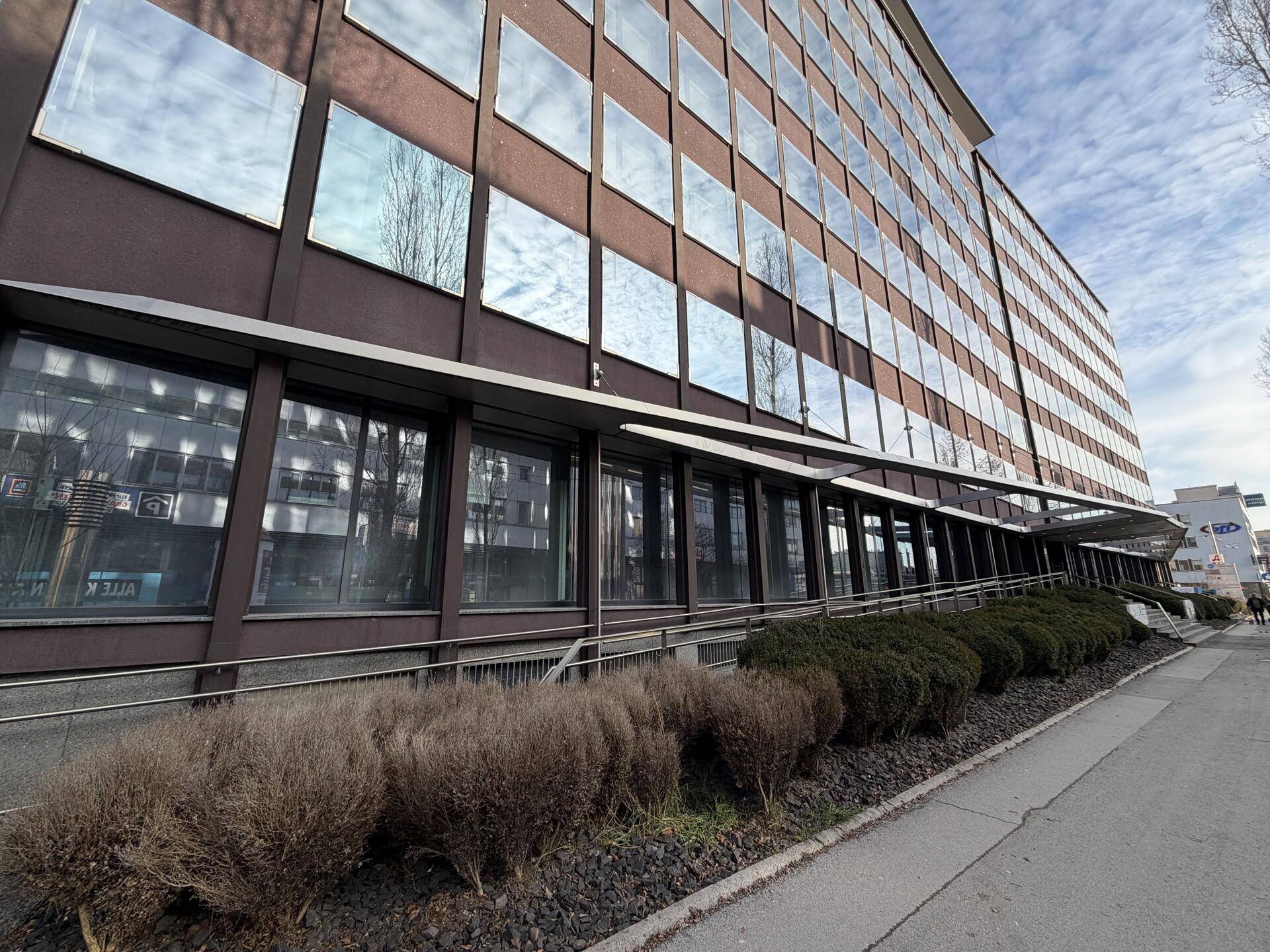 Moderne Bürogebäude-Fassade mit reflektierenden Fenstern und einer seitlichen Rampe für Barrierefreiheit.