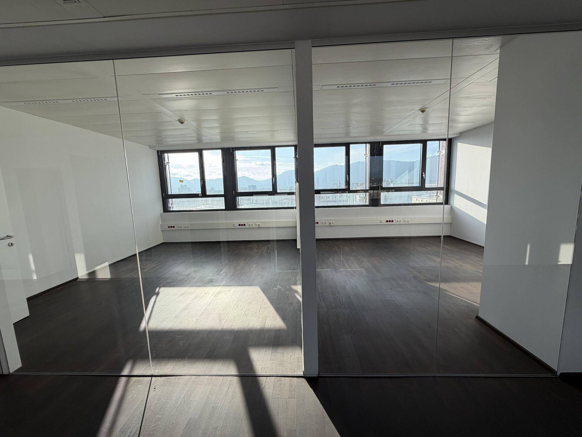 Helles Büro mit Glaswänden, dunklem Holzboden und weitem Blick durch die Fenster.