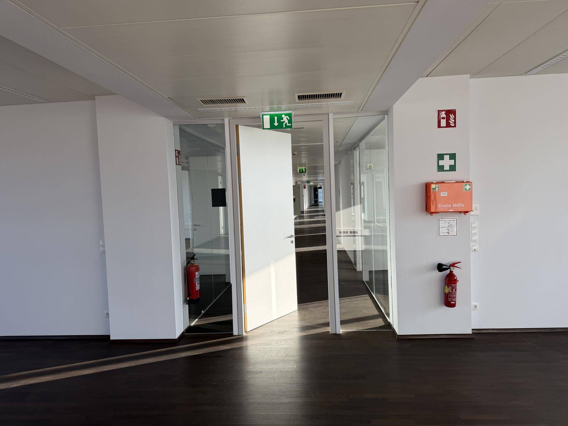 Büroflur mit Glaswänden, dunklem Holzboden und Brandschutzvorrichtungen.