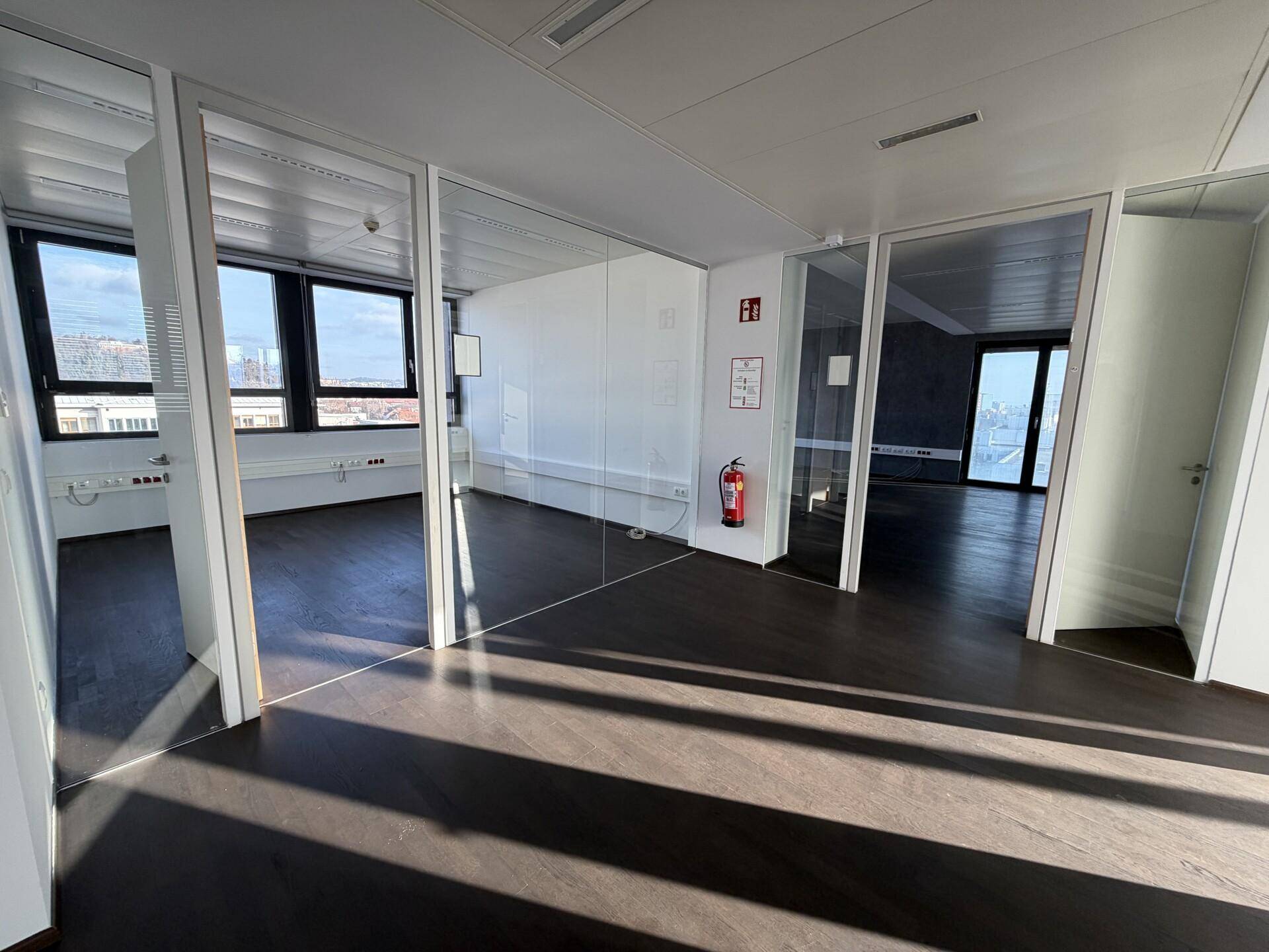 Helles Büro mit Glaswänden, dunklem Holzboden und Blick auf die Stadt.