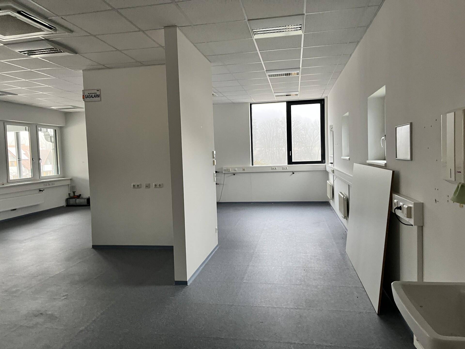 Geräumiges Büro mit Trennwänden, großen Fenstern und dunklem Bodenbelag, ideal für flexible Nutzung.