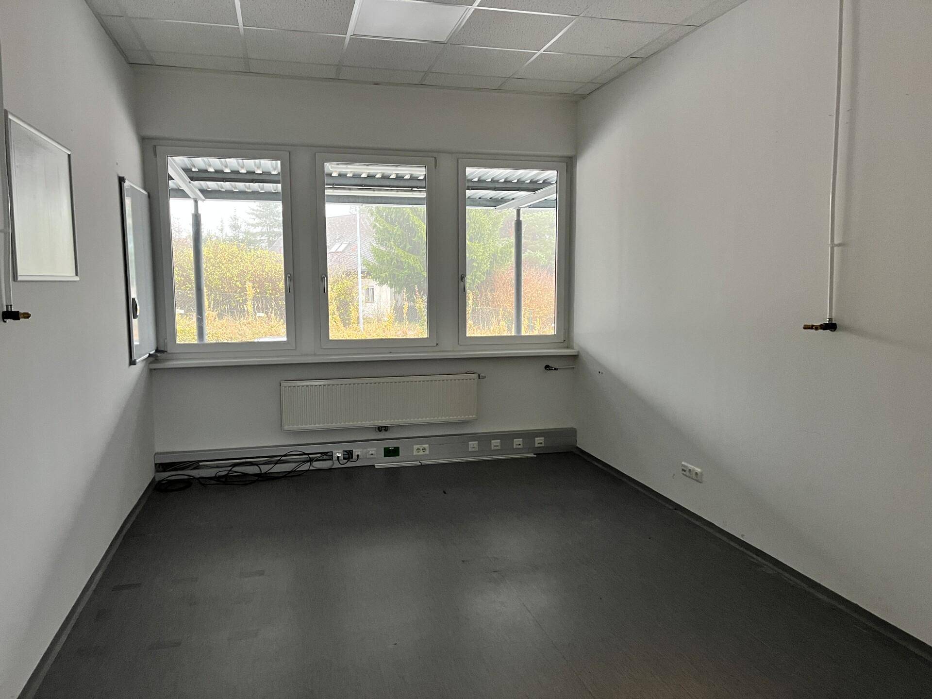 Leeres Büro mit drei Fenstern, Heizkörper und dunklem Bodenbelag, bereit zur individuellen Gestaltung.