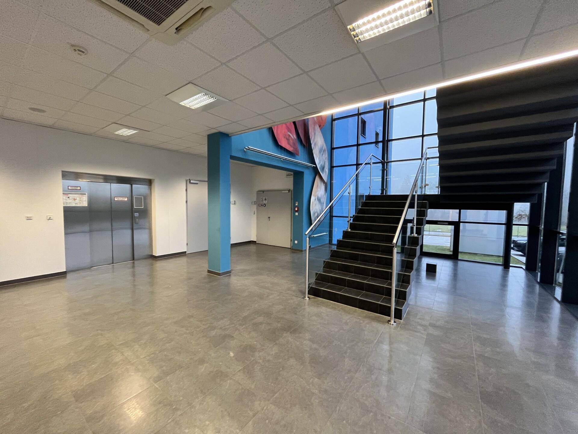 Geräumige Eingangshalle mit Fliesenboden, Aufzügen und einer modernen Treppe mit Glasfront.