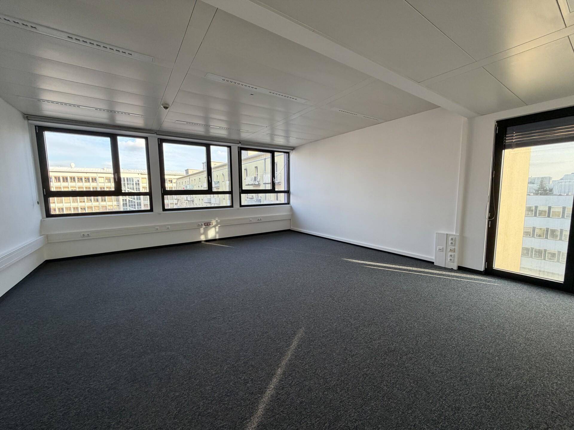 Geräumiger Büroraum mit großen Fenstern, die viel Tageslicht hereinlassen und einen Blick auf die Stadt ermöglichen.