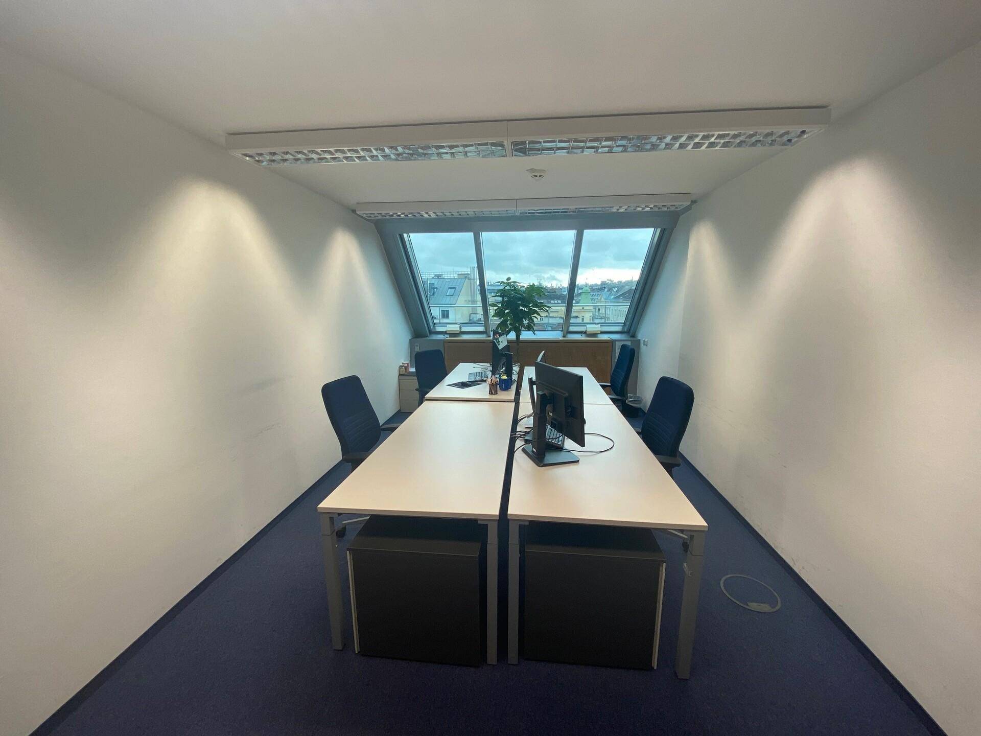 Büroraum im Dachgeschoss mit schrägen Fenstern, die einen weiten Blick über die Stadt bieten.