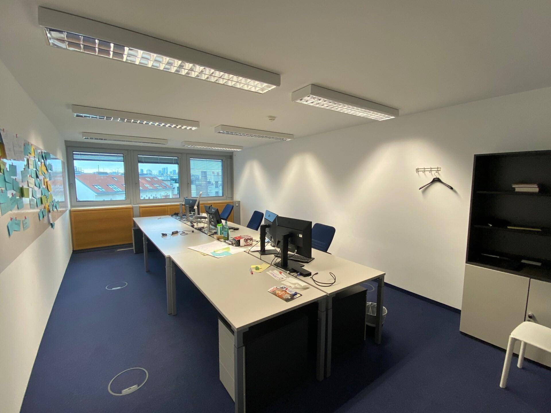 Geräumiger Bürobereich mit mehreren Arbeitsplätzen, Computern und Fenstern, die viel Tageslicht hereinlassen.