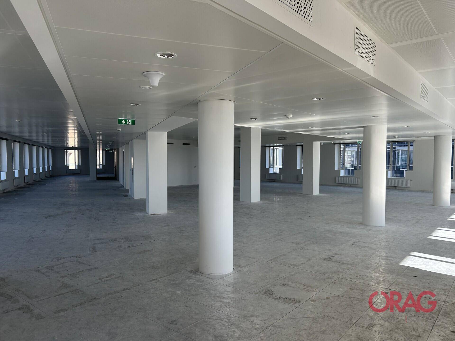 Heller, weitläufiger Büroraum mit Säulen, abgehängter Decke und Lüftungssystemen.