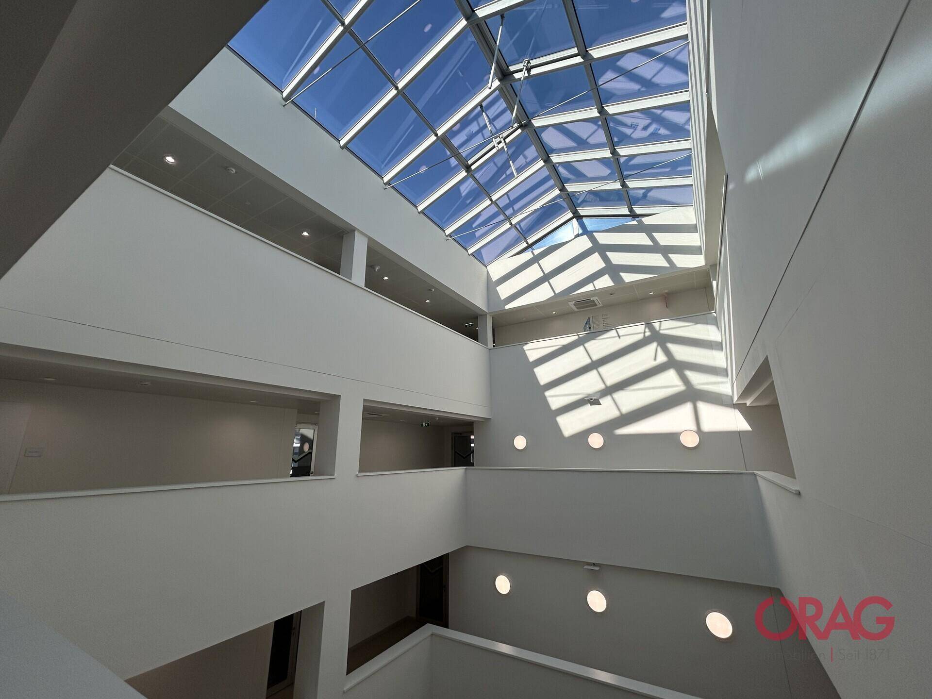 Helles Atrium mit beeindruckendem Glasdach, das viel natürliches Licht in das Gebäude bringt.