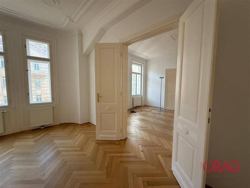 Helles Zimmer mit klassischem Fischgrätparkett und hohen Doppeltüren, die zu einem weiteren Raum führen.