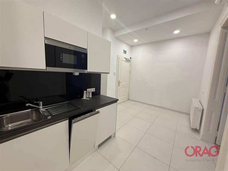 Moderne Küchenzeile mit weißen Schränken, integrierter Mikrowelle und Spülbecken in einem hellen Raum.