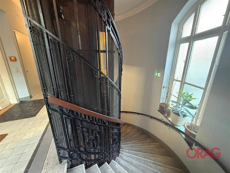 Historisches Treppenhaus mit schmiedeeisernem Geländer und einem großen Fenster, das den Bereich erhellt.