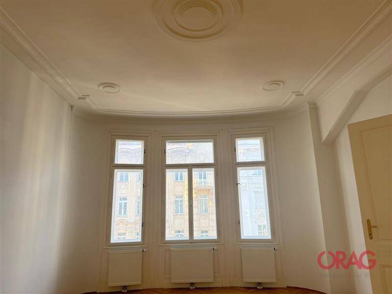 Detailansicht der hohen Decke mit Stuckverzierungen und der großen Fensterfront, die den Raum erhellt.