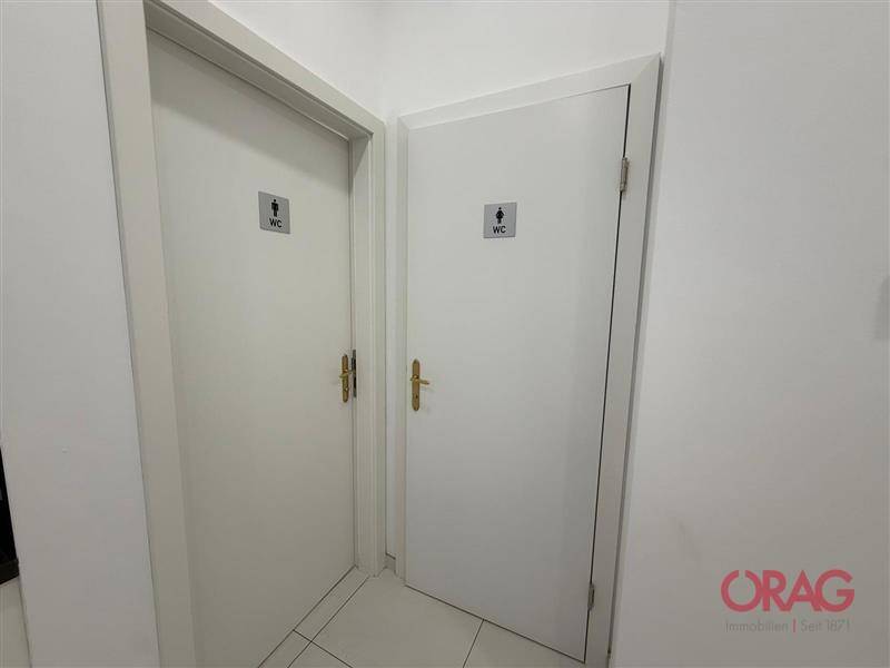 Zwei separate Toilettenkabinen mit weißen Türen und WC-Schildern in einem schlichten Flur.