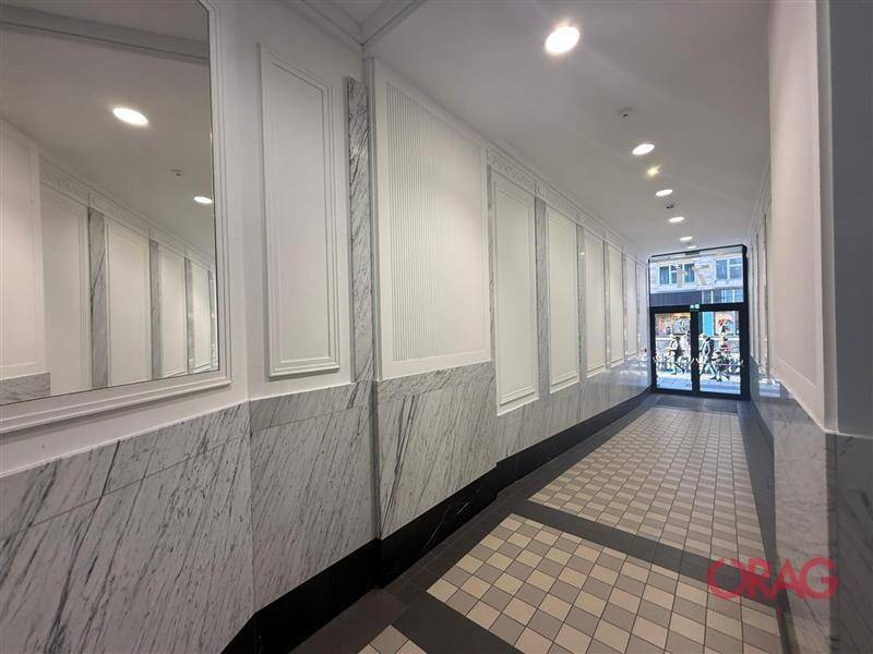 Eleganter Flur mit Marmorverkleidung an den Wänden, gemustertem Fliesenboden und Blick zur Eingangstür.