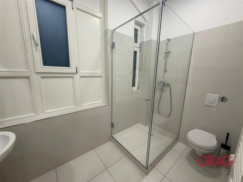 Modernes Badezimmer mit Duschkabine aus Glas, wandhängendem WC und Fenster für natürliche Belüftung.