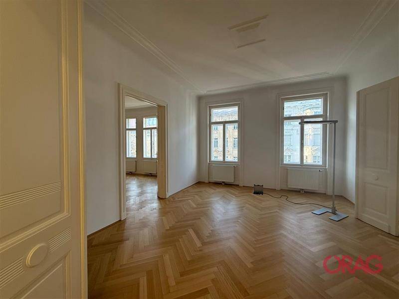 Geräumiger Raum mit Fischgrätparkett und hohen Fenstern, die einen Blick auf die umliegenden Gebäude bieten.