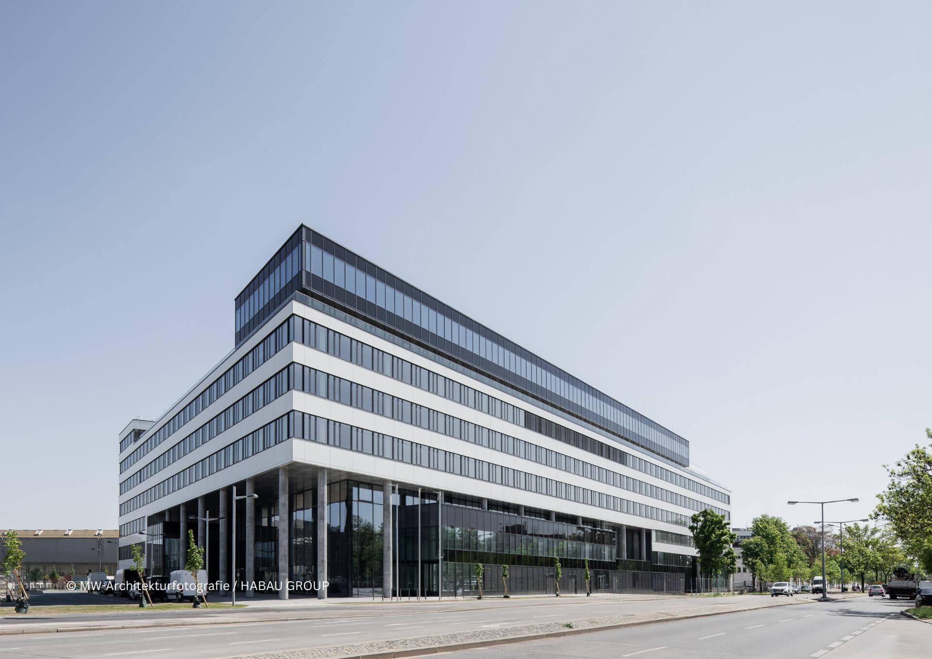 Modernes Bürogebäude mit markanter Architektur, großen Glasflächen und klaren Linien unter blauem Himmel.