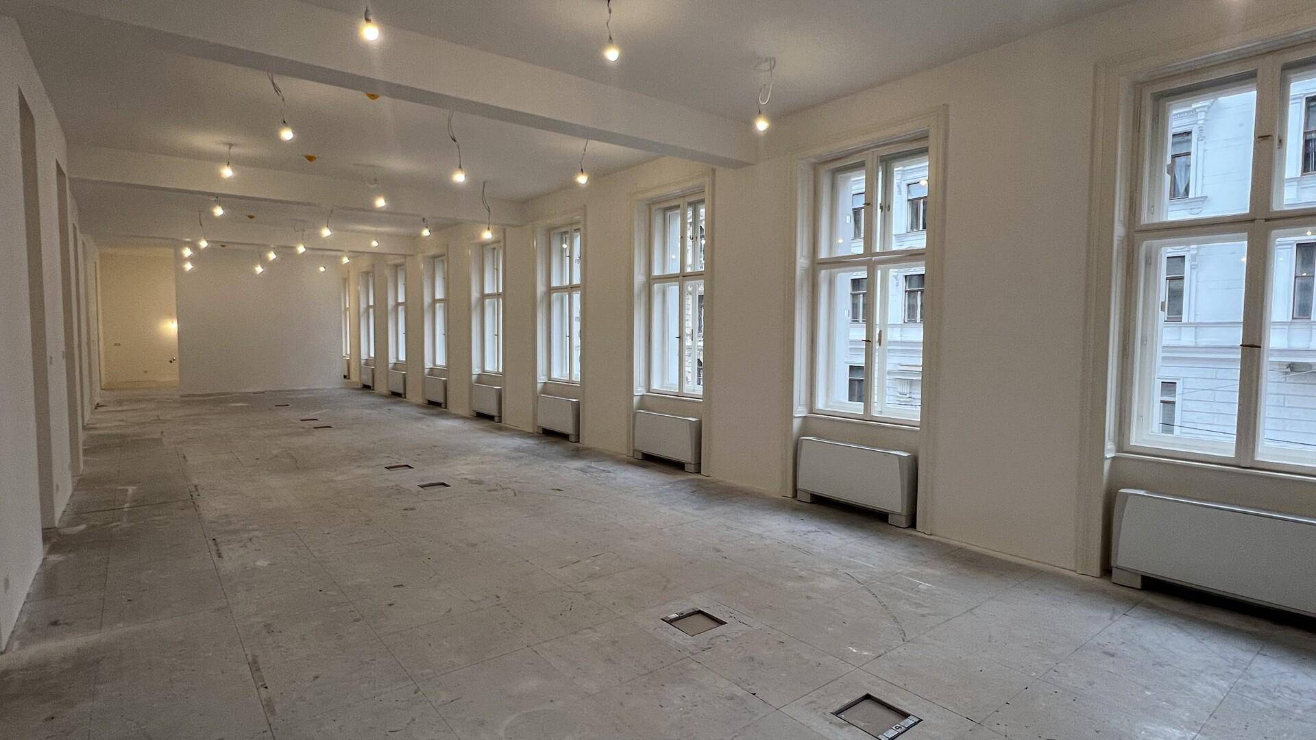 Geräumiger, heller Bürobereich mit vielen Fenstern und einem vorbereiteten Betonboden für den Endausbau.