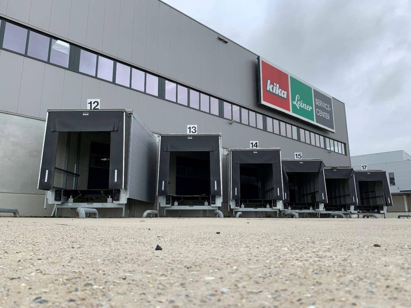 Außenansicht eines modernen Logistikzentrums mit mehreren Laderampen und Firmenbeschilderung.