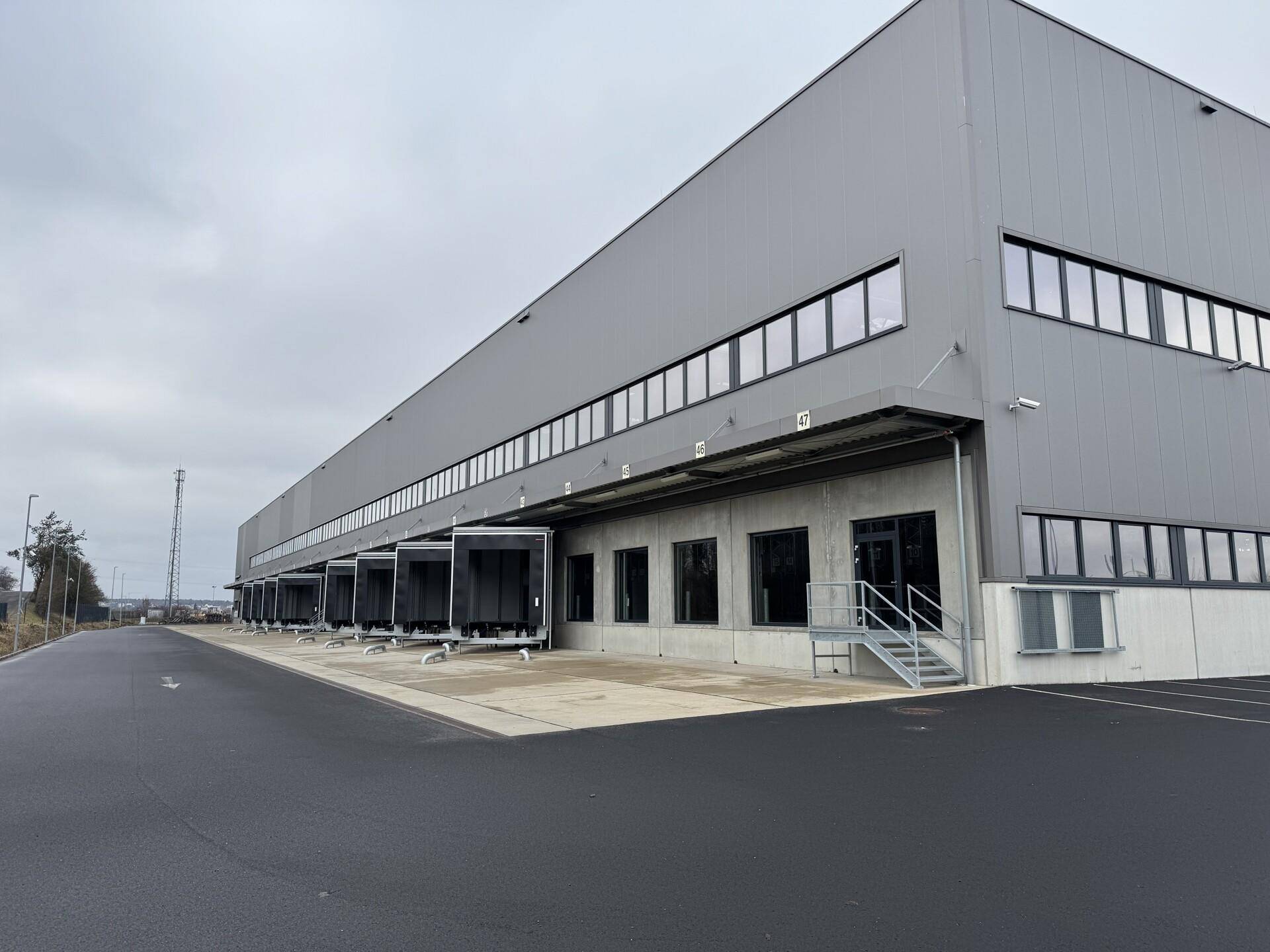 Moderne Industriefassade mit zahlreichen Laderampen und großen Fenstern unter bewölktem Himmel.